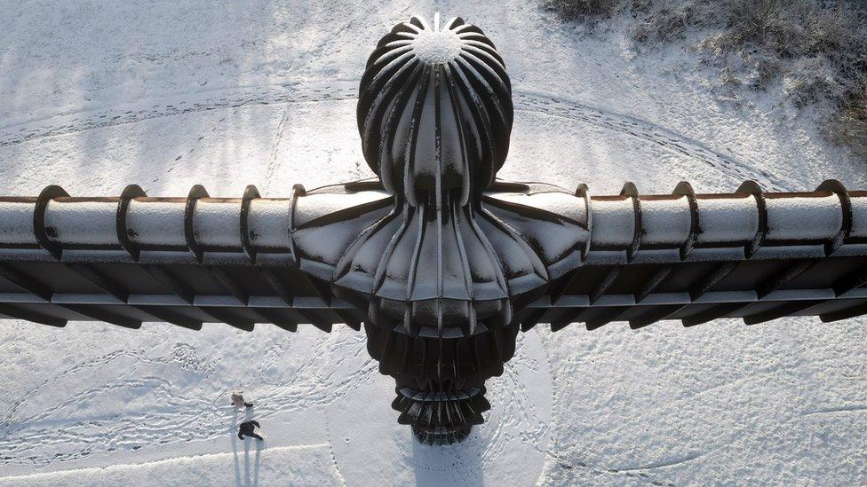 An aerial shot of The Angel of the North statue in Gateshead covered in snow, with walkers near its base