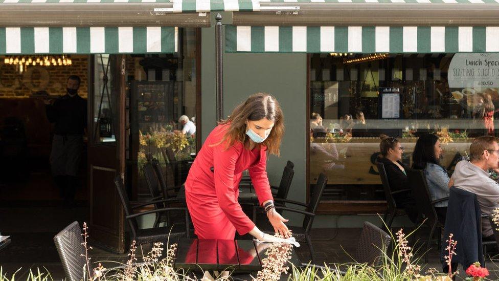 A waitress cleans a table outside a restaurant in Soho, London