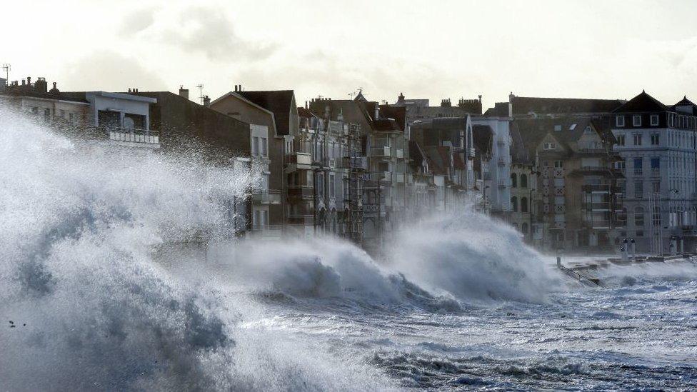 A wave crashes against the sea wall in