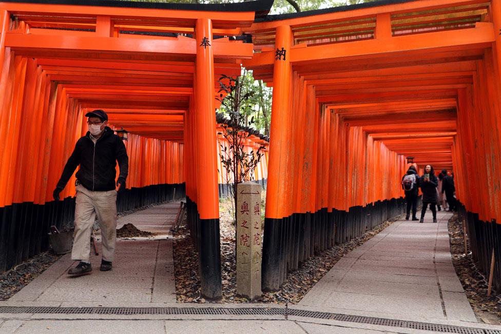 A construction man wears a face mask while walking through the empty Torii gates of Fushimi Inari Taisha Shrine that are usually overrun by tourists on March 06, 2020 in Kyoto, Japan