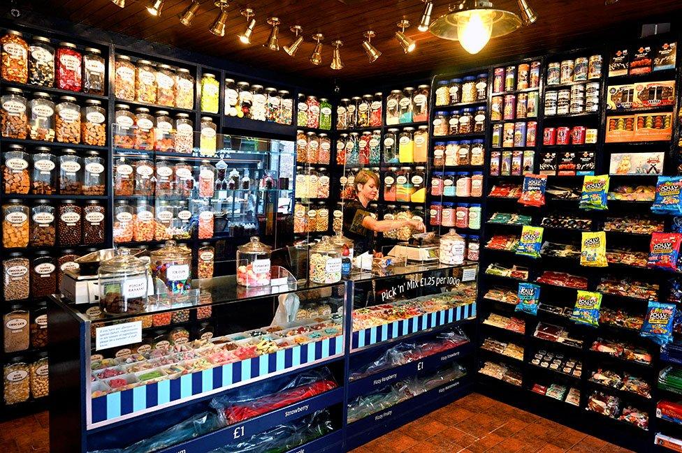 A shop worker stands behind a screen in a sweet shop