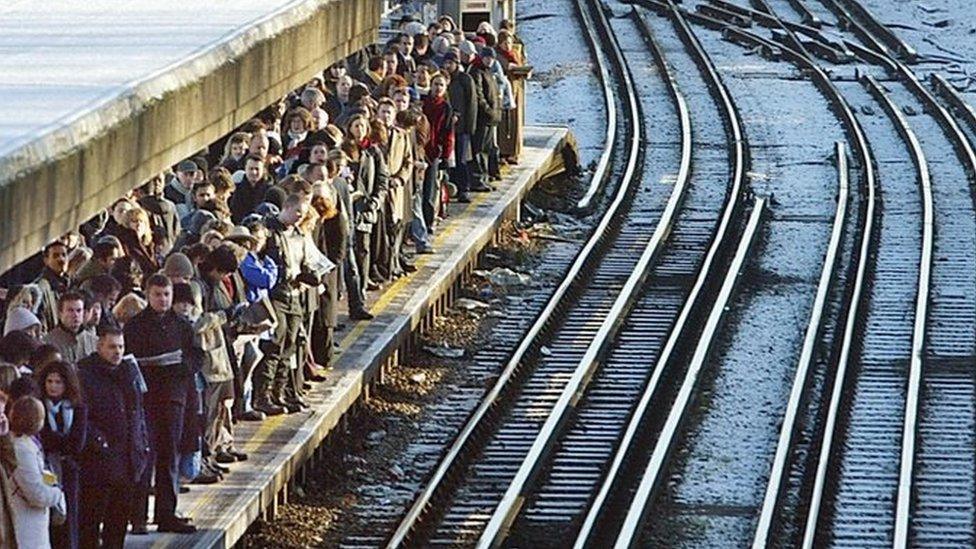 Passengers crowd onto a platform beside train tracks