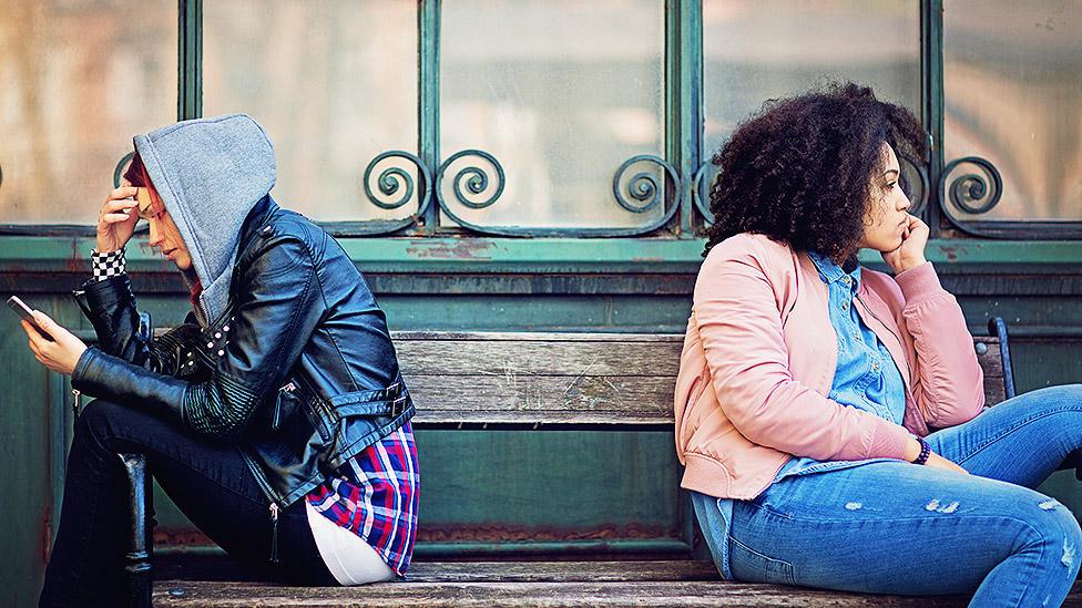 Two women ignoring each other on a park bench