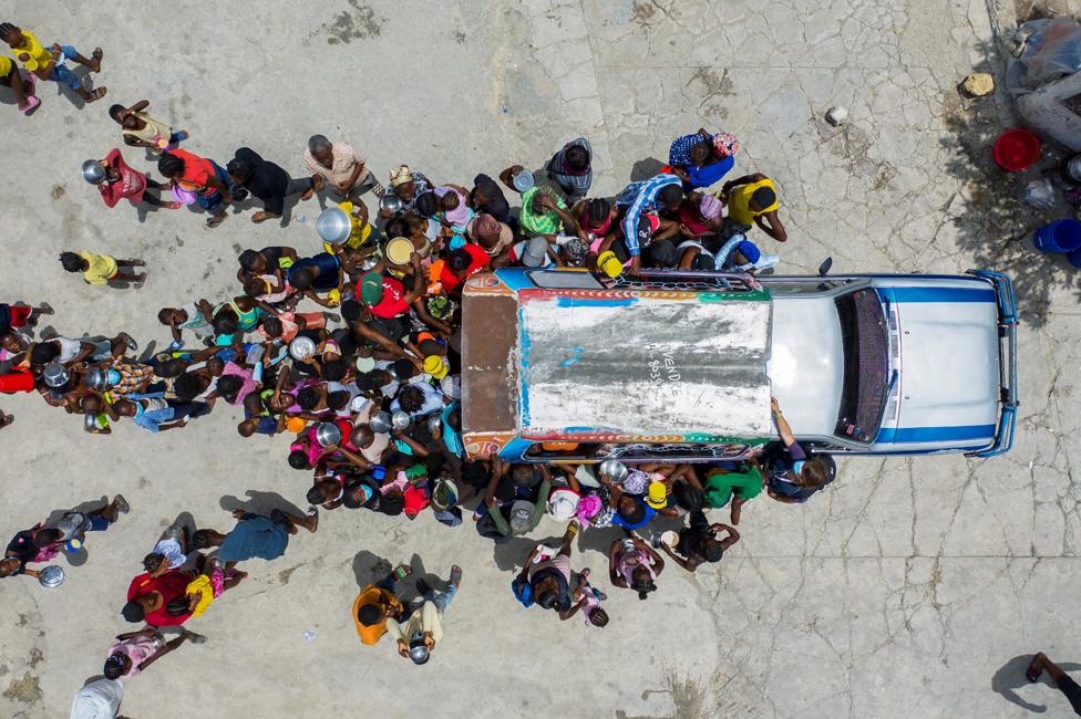 People gather around a car where volunteers distribute food to refugees at a shelter for families displaced by gang violence at the Saint Yves Church in Port-au-Prince, Haiti July 26, 2021.