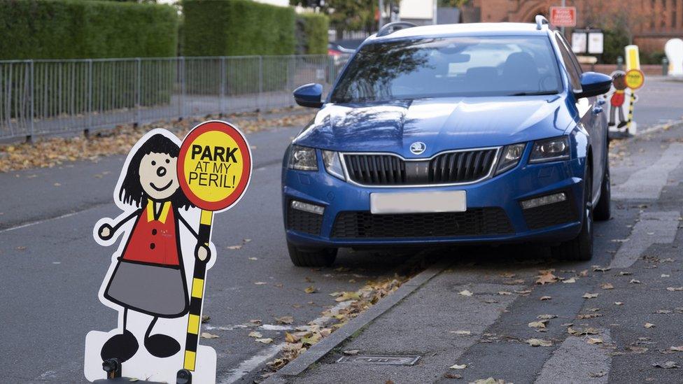 Car parked on pavement with sign saying 'park at my peril'