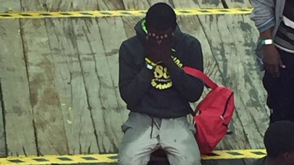 Survivor kneels on the floor and holds his head in his hands