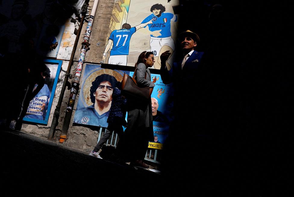 People walk past murals of former footballer Diego Maradona in the Spanish quarter of Naples before the match