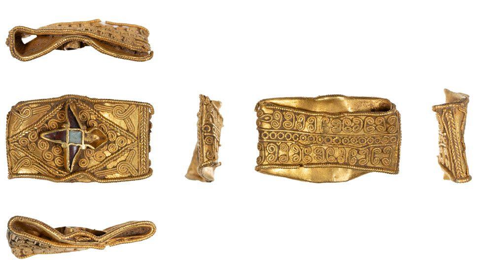 Six views of a squashed Anglo-Saxon gold ring. Its front has a four-point star in the middle with a square blue gem stone in its middle. It is covered in fine scroll work also in gold. The back is covered in tiny scrolls and circles of gold. The other four views of are its squished sides