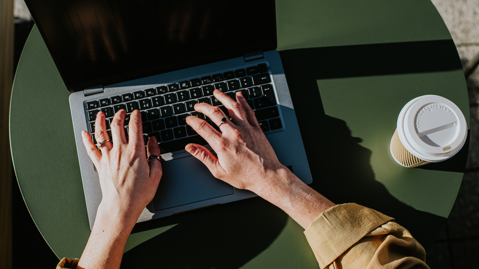 A person using a laptop, with a cup of coffee next to them