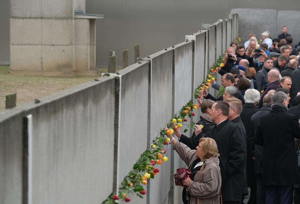 People stick flowers into slats of a still-standing section of the Berlin Wall, following a ceremony to celebrate the 30th anniversary of the fall of the wall in 1989.