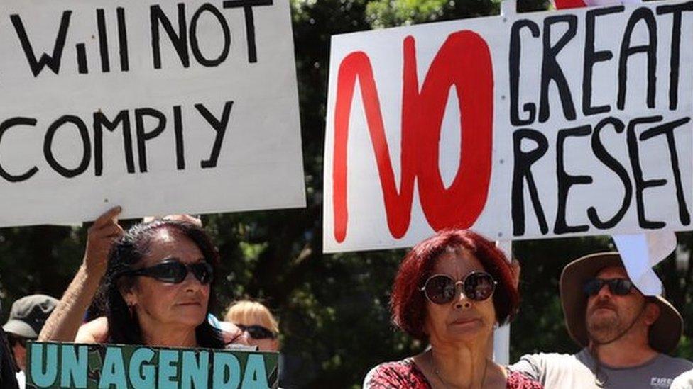 People hold placards protesting the United Nations and the "great reset" at a rally of conspiracy theorists and supporters of US President Donald Trump on January 14, 2021 in Wellington, New Zealand