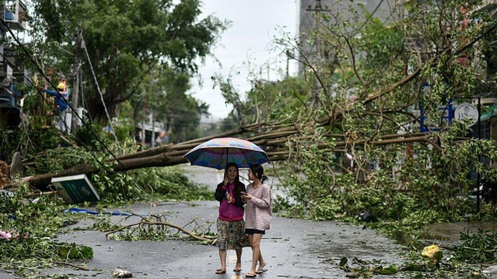 Women walk past uprooted trees in central Vietnam's Quang Ngai province