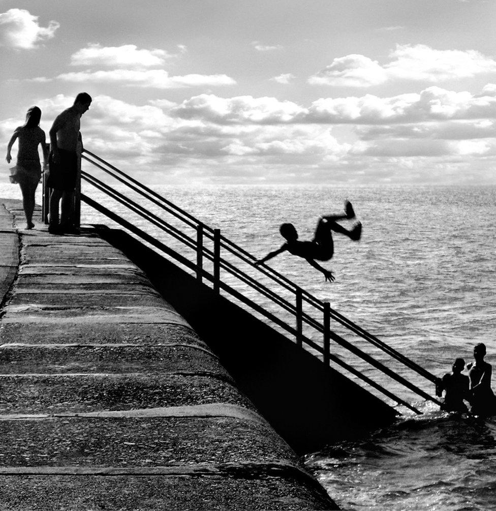 A boy somersaults from the promenade into the sea