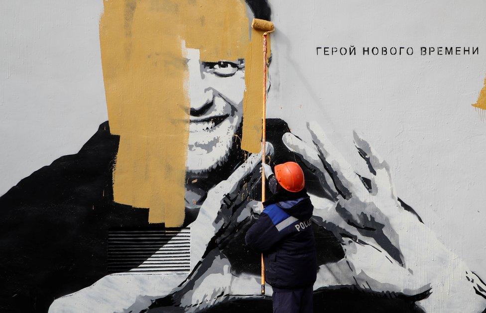 A worker paints over a mural depicting Alexei Navalny in St Petersburg