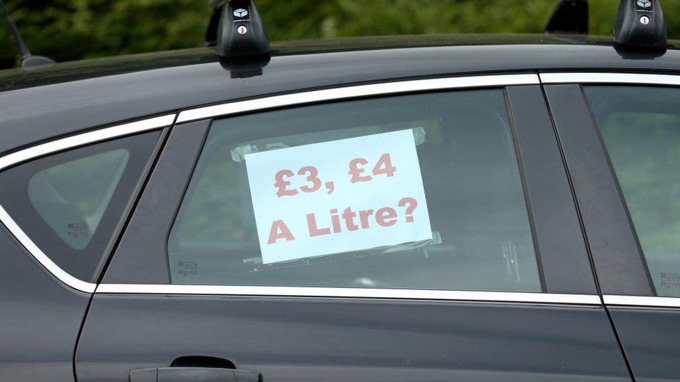 a car window with a sign taped to its inside that reads £3, £4 a litre