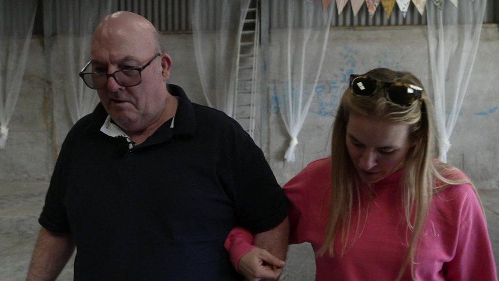 Roger and Jessie walking arm in arm in a barn.