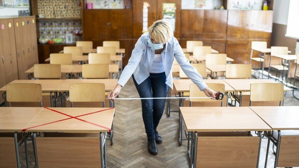 Woman in face mask measuring space between desks