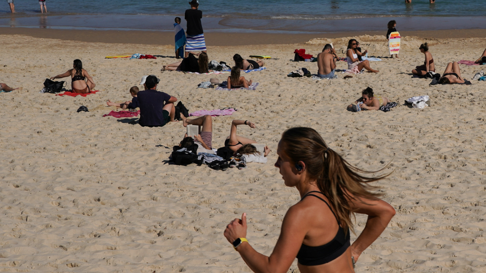 Jogger runs down Bondi Beach past groups sunbathing on the sand