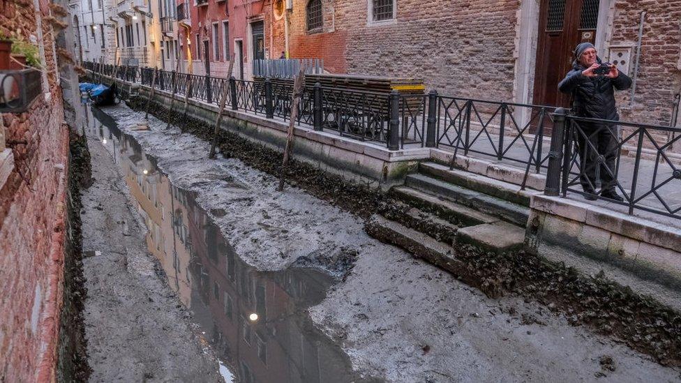 canal in venice running dry with man taking photo