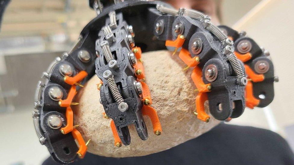 A man holds a robot claw gripping a rock