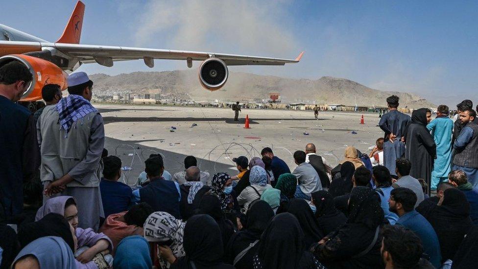 Afghan people sit as they wait to leave the Kabul airport