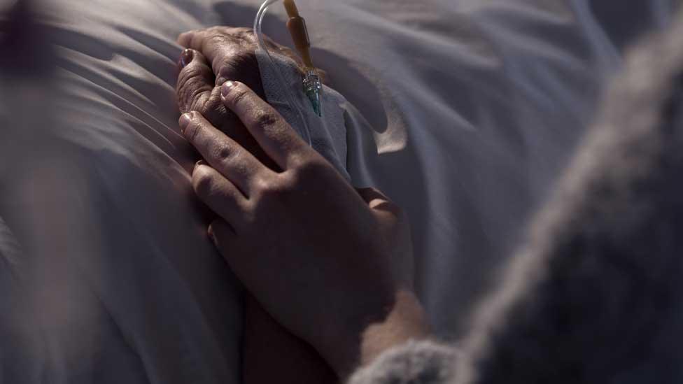 A woman's hand holding another's in a hospital bed