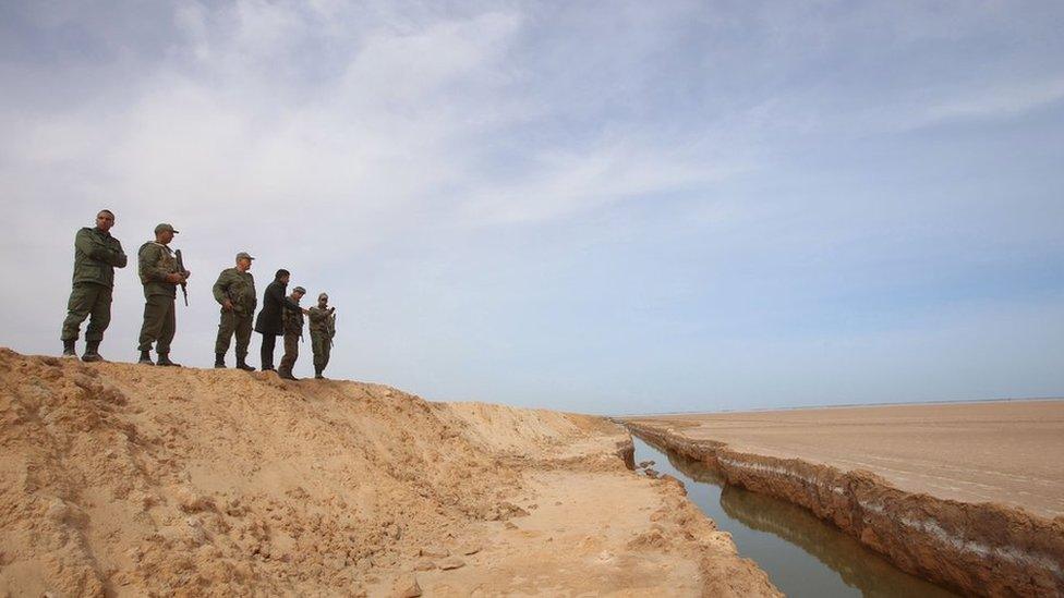 Soldiers overlook a trench, that forms part of a barrier along the frontier with Libya, in Sabkeht Alyun