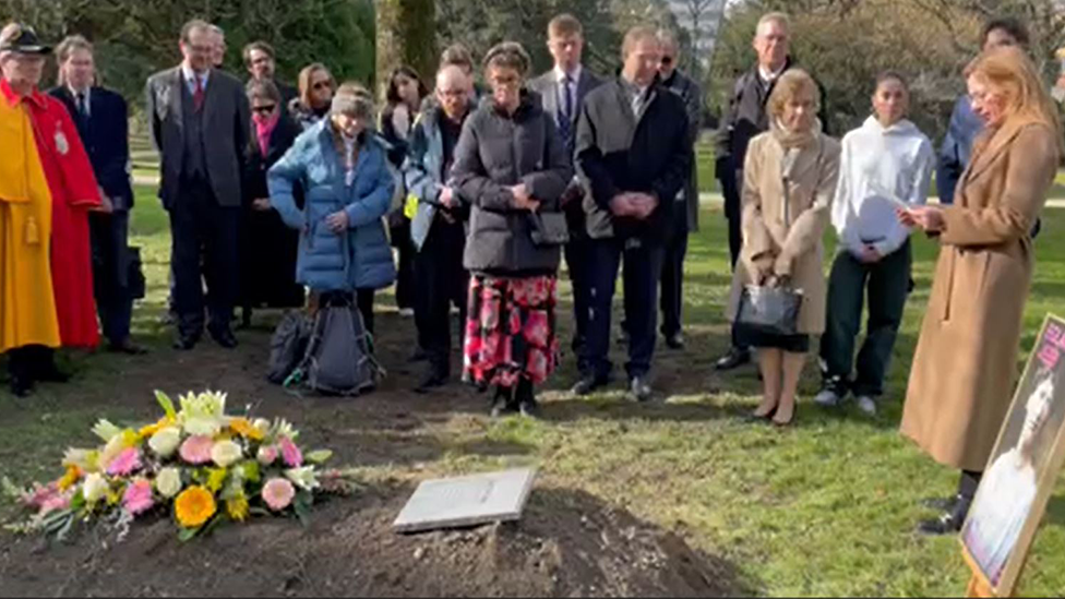 Crowd gathers around the grave