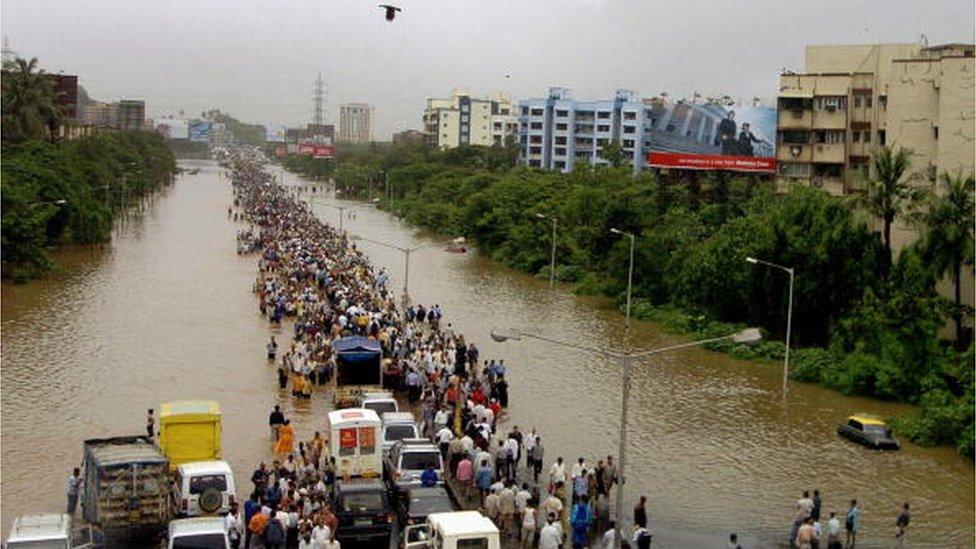 MUMBAI, INDIA: Indian commuters walk through floodwaters past stranded motor vehicles after heavy torrential rains paralysed the city of Mumbai