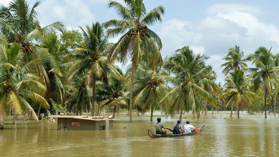 Three people riding a boat through a flooded area