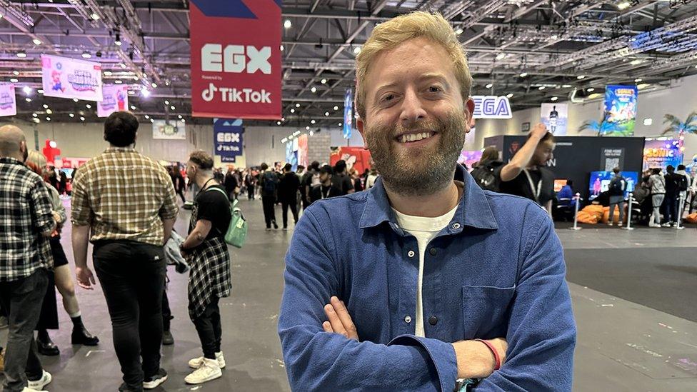 A man in a blue shirt stands in a big convention centre hall