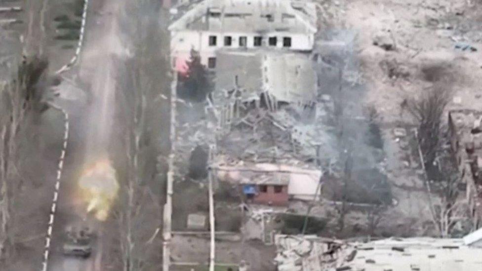 Tank shoots weapon surrounded by demolished buildings