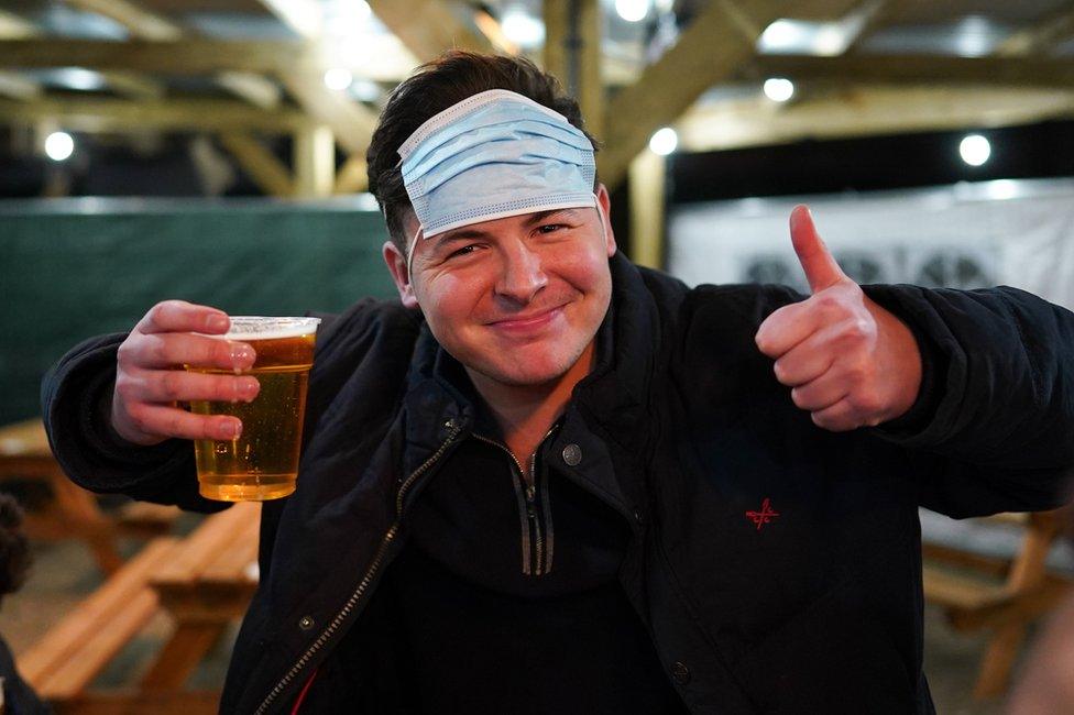 A man holds a pint of beer with a face mask on his head