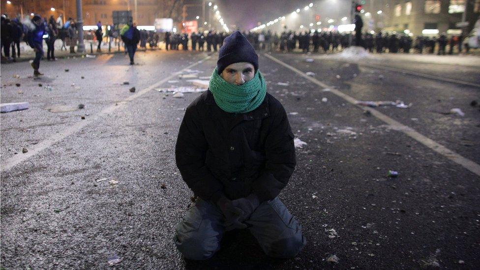 A protestor sits on the ground following scuffles between protestors and Romanian police at a demonstration in Bucharest, Romania