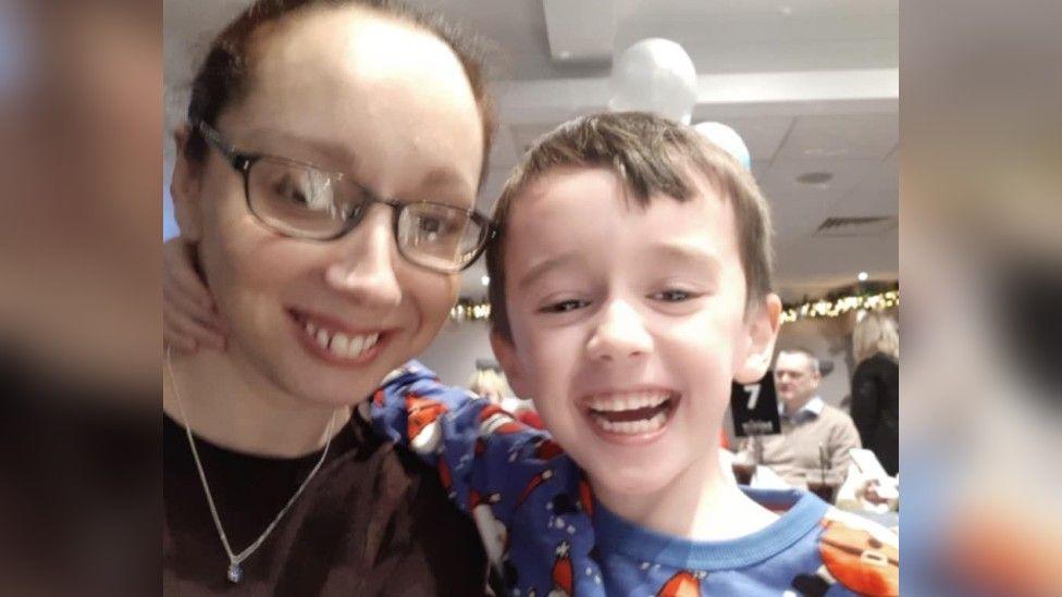 Claire Hannah and her son Anton smile for a photograph at the OKE Christmas event. Anton can be seen beaming as he wears Christmas-themed clothes. 