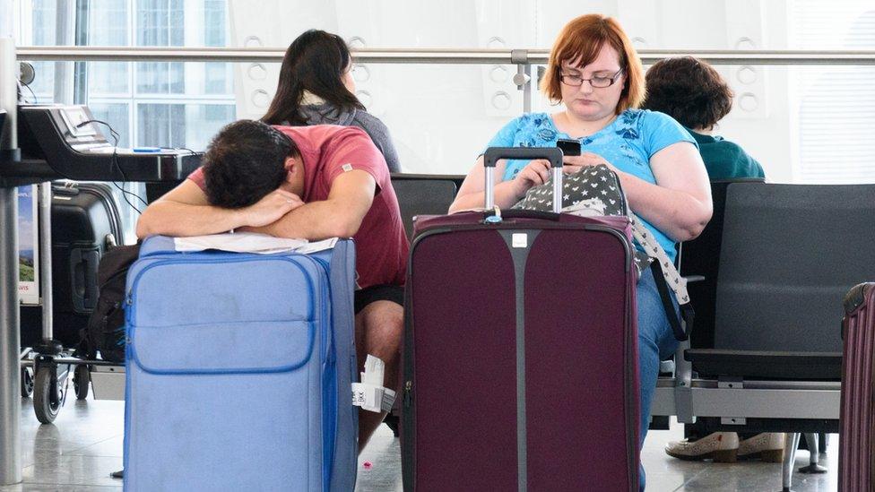 Passengers sleep and sit inside Heathrow airport Terminal 5 waiting for their flights.