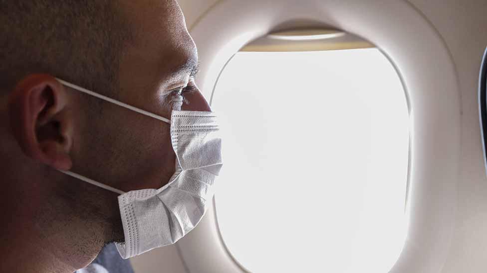 Man in mask in window seat on plane