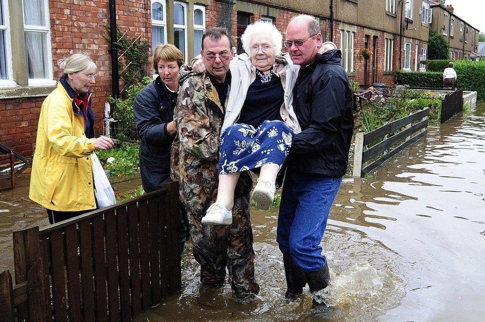 An elderly resident is carried to safety from a flooded street