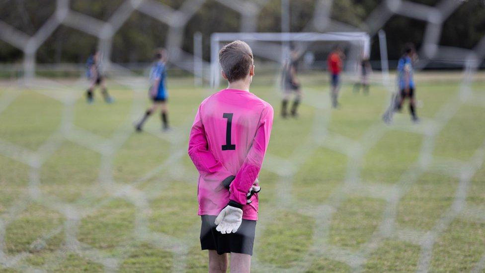 boy-standing-in-front-of-football-net.