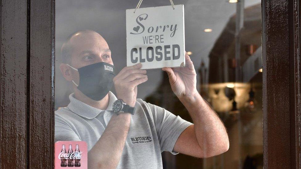 A man puts a "closed" sign in the window of his cafe