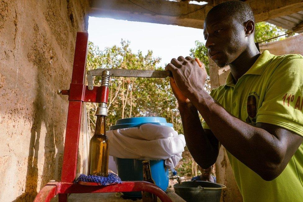 On Kumus Da Silva's local small scale cashew juice creation site, after workers sift out cashew juice they bottle and stamp the bottles before it is warmed in metal barrels to prevent fermentation.