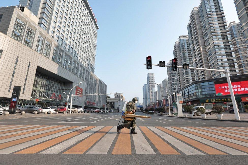 A worker with sanitising equipment crosses the road in front of a hospital in Yichang city of Hubei