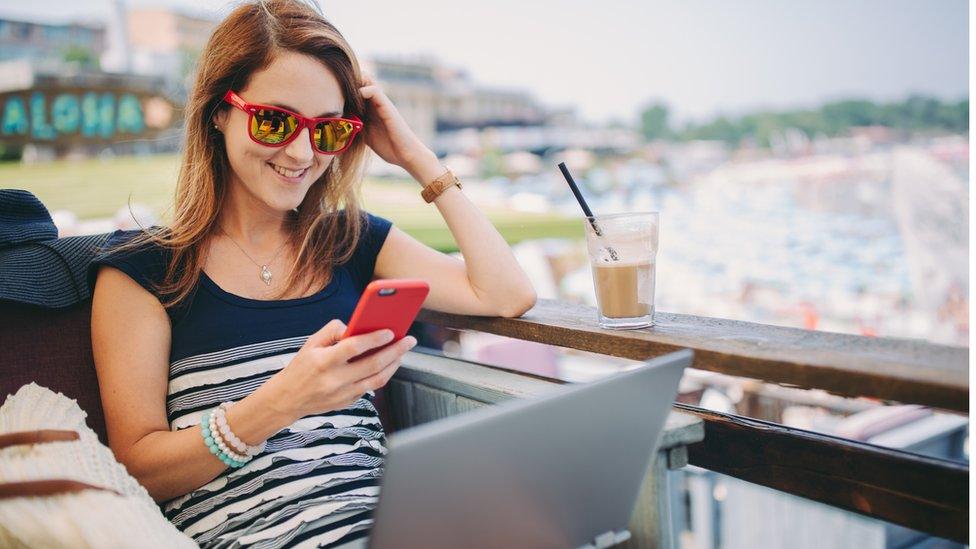 Woman sat at a balcony with laptop and phone