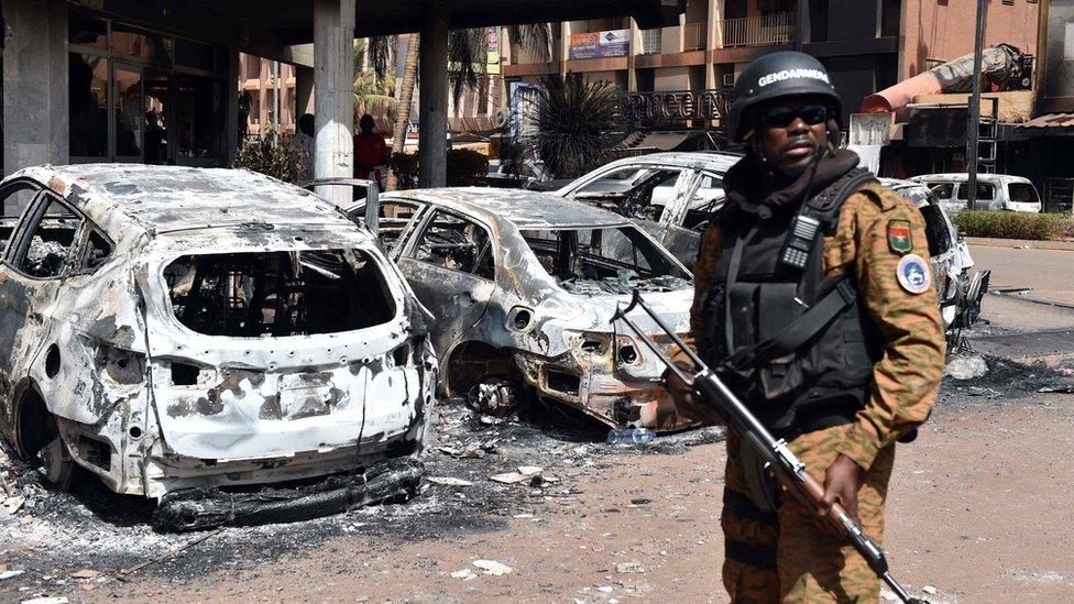 Burkina Faso official stands guard next to burnt cars outside hotel attacked in Ouagadougou