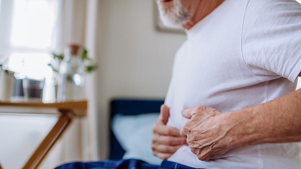 Man holds stomach on bed