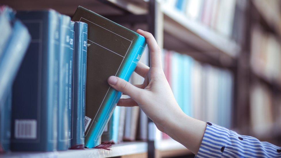 A hand pulls a book from a shelf filled with other blue books