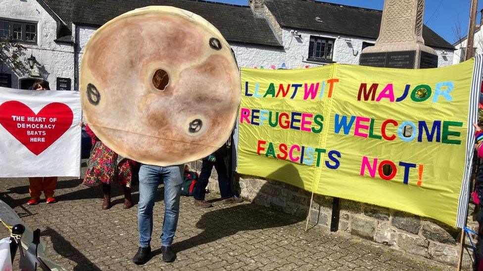 Baner yn dweud fod Llanilltud Fawr yn croesawu ffoaduriaid a rhywun wedi gwisgo fel pice ar y maen