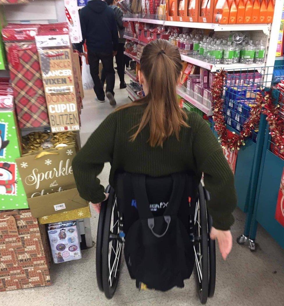 Charlotte trying to squeeze through a narrow aisle in her wheelchair