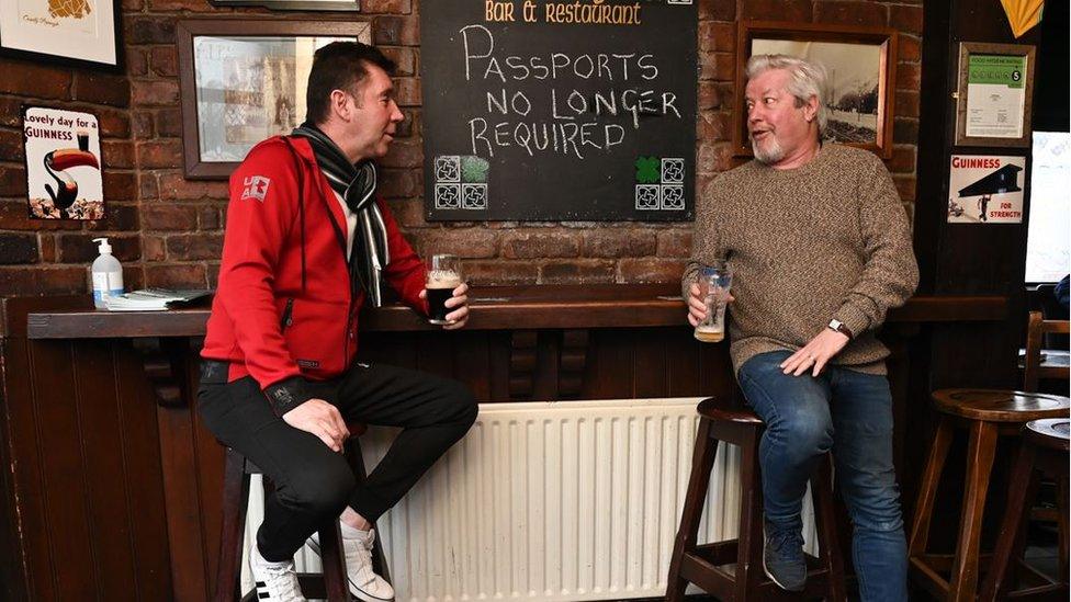 Two men standing at the bar with a sign saying Covid passports are no longer required