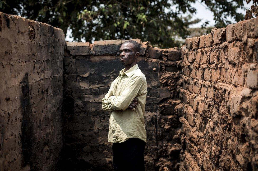 Emmanuel stands in front of the remains of his house.